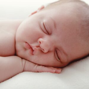 Gros plan d'un bébé qui dort avec la main sous la joue, sur une couverture blanche