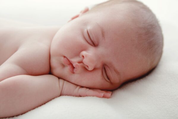 Gros plan d'un bébé qui dort avec la main sous la joue, sur une couverture blanche