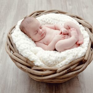 Bébé qui dort sur une couverture en laine blanche dans un panier en osier posé sur un sol en parquet