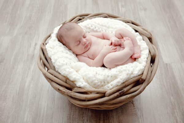 Bébé qui dort sur une couverture en laine blanche dans un panier en osier posé sur un sol en parquet